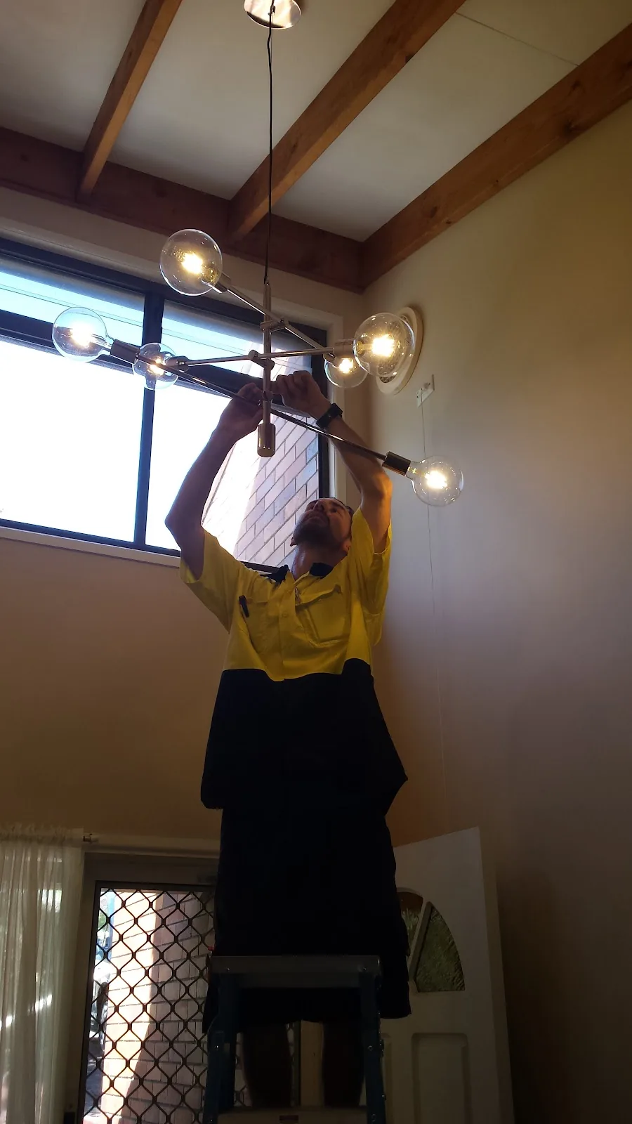 Sparky 4 You electrician on a ladder fitting a glass globe chandelier