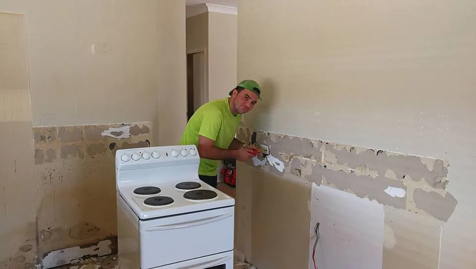 Electrician in hi-vis connecting a freestanding electric cooker in a kitchen being renovated