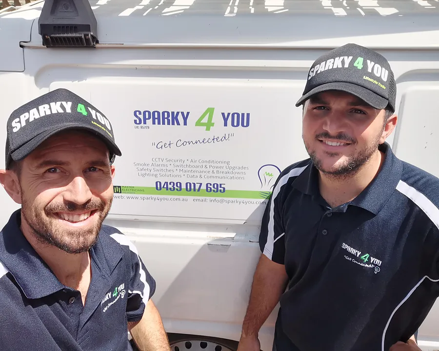 Two Sparky 4 You electricians in branded caps and polos, smiling beside the company van