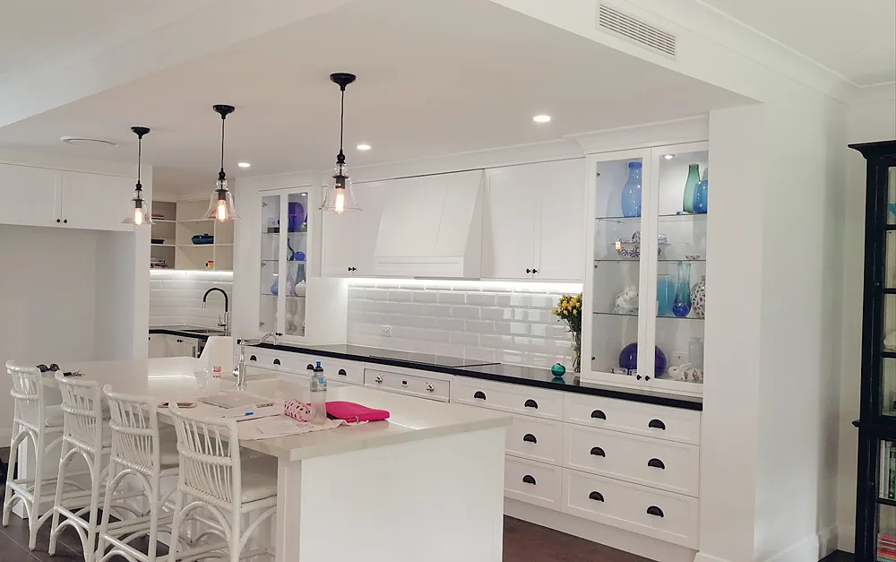 White kitchen with three pendant lights over the island and LED downlights